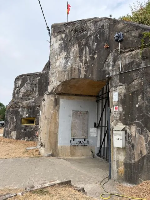 Weathered concrete entrance bunker of Fort Eben-Emael with a barred gate and memorial plaque